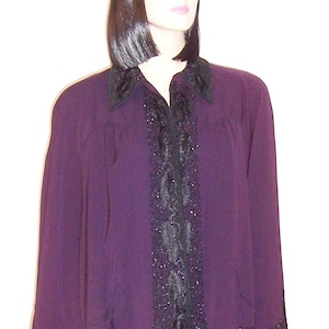 May include: A purple blouse with a black lace trim and a black collar. The blouse has a long sleeve and a button-up front.