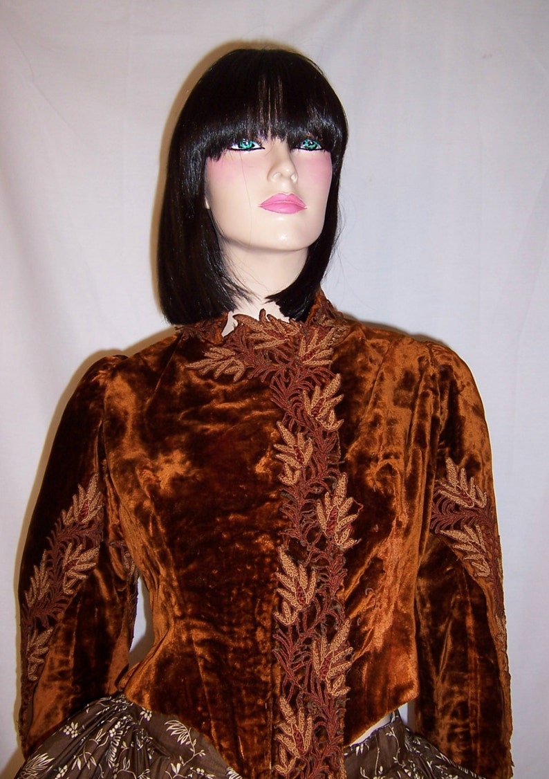 May include: A brown velvet jacket with intricate gold embroidery. The jacket has a high neckline and long sleeves. The embroidery is in a floral pattern.