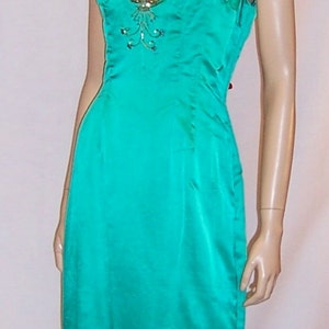 May include: A teal satin evening gown with gold and silver embellishments. The gown has a V-neckline and a fitted bodice. The skirt is full-length and has a slight train.