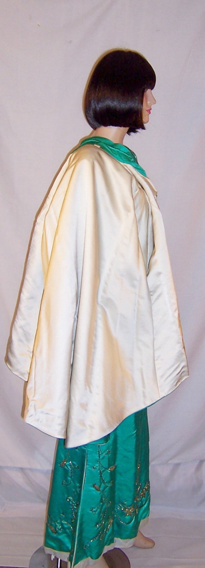 May include: A white satin cape with a green satin collar over a teal satin skirt with gold embroidery.