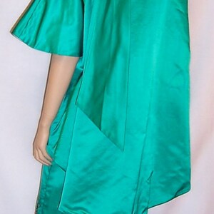 May include: A teal green satin dress with a long, flowing cape. The dress has a fitted bodice and a full skirt with gold embroidery.
