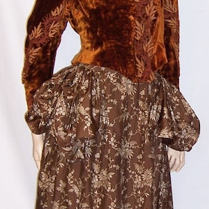 May include: A brown velvet jacket with gold embroidery over a brown floral print skirt. The jacket has a high neckline and long sleeves. The skirt is full and flowing.