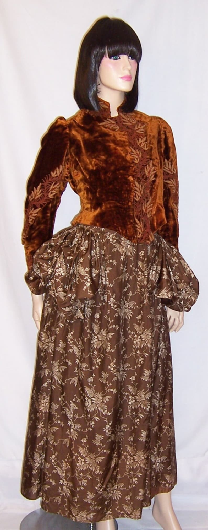 May include: A brown velvet jacket with gold embroidery over a brown floral print skirt. The jacket has a high neckline and long sleeves. The skirt is full and flowing.