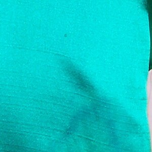 May include: A close-up of a teal green fabric with a subtle sheen. The fabric has a smooth, silky texture.