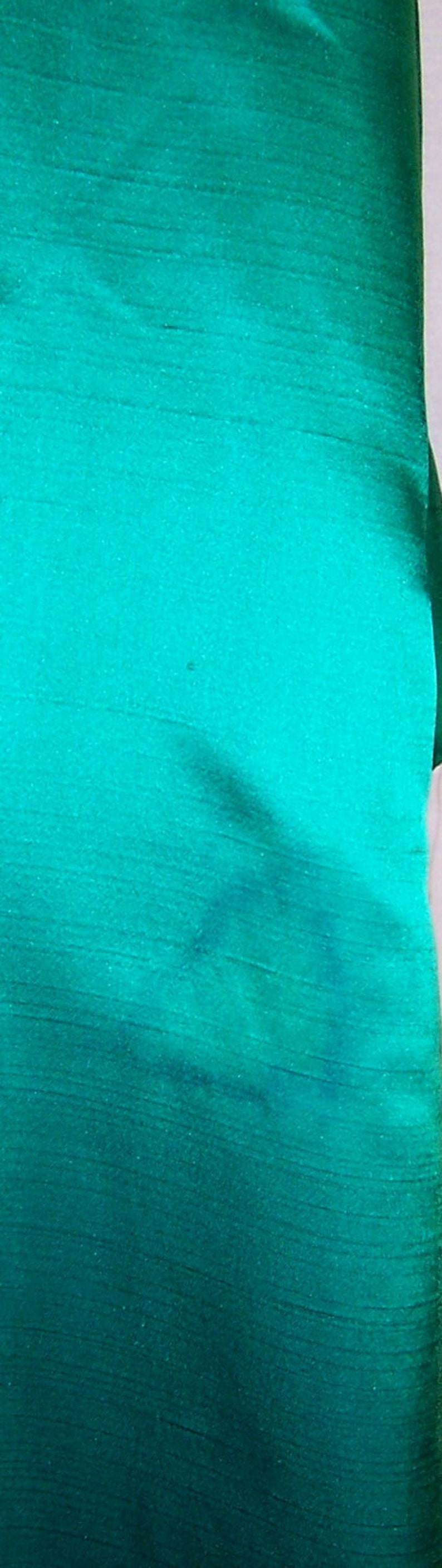 May include: A close-up of a teal green fabric with a subtle sheen. The fabric has a smooth, silky texture.