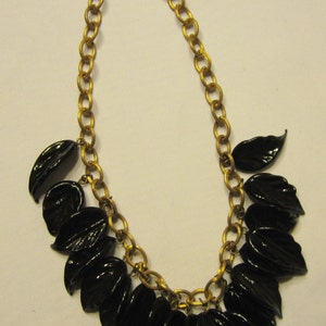 May include: A gold-tone chain necklace featuring glossy black leaf pendants. The necklace has a classic design with a series of oval links forming the chain. The black leaves are evenly spaced and add a touch of nature-inspired elegance to the jewelry.