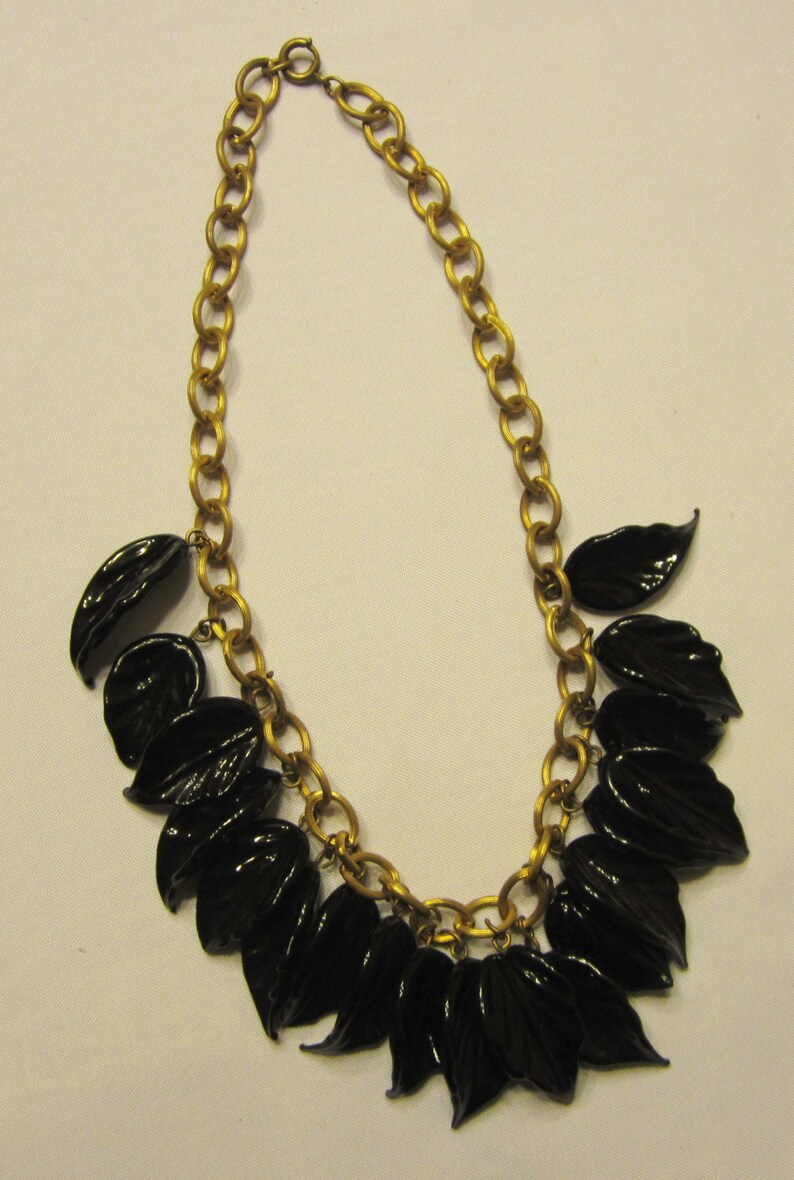 May include: A gold-tone chain necklace featuring glossy black leaf pendants. The necklace has a classic design with a series of oval links forming the chain. The black leaves are evenly spaced and add a touch of nature-inspired elegance to the jewelry.