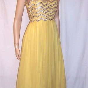 Puede incluir: Un vestido amarillo sin mangas con un corpiño de lentejuelas y una falda fluida. El vestido está en un maniquí con el pelo negro corto.