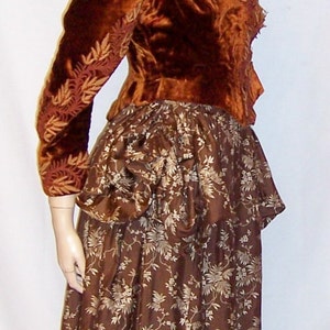 May include: A brown velvet jacket with gold embroidery over a brown skirt with a floral pattern.
