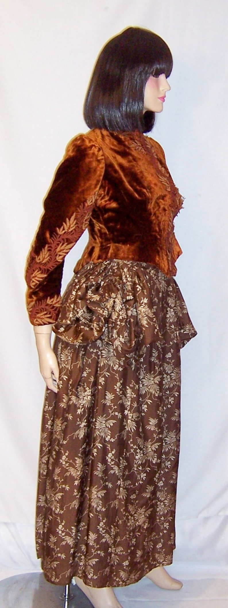 May include: A brown velvet jacket with gold embroidery over a brown skirt with a floral pattern.