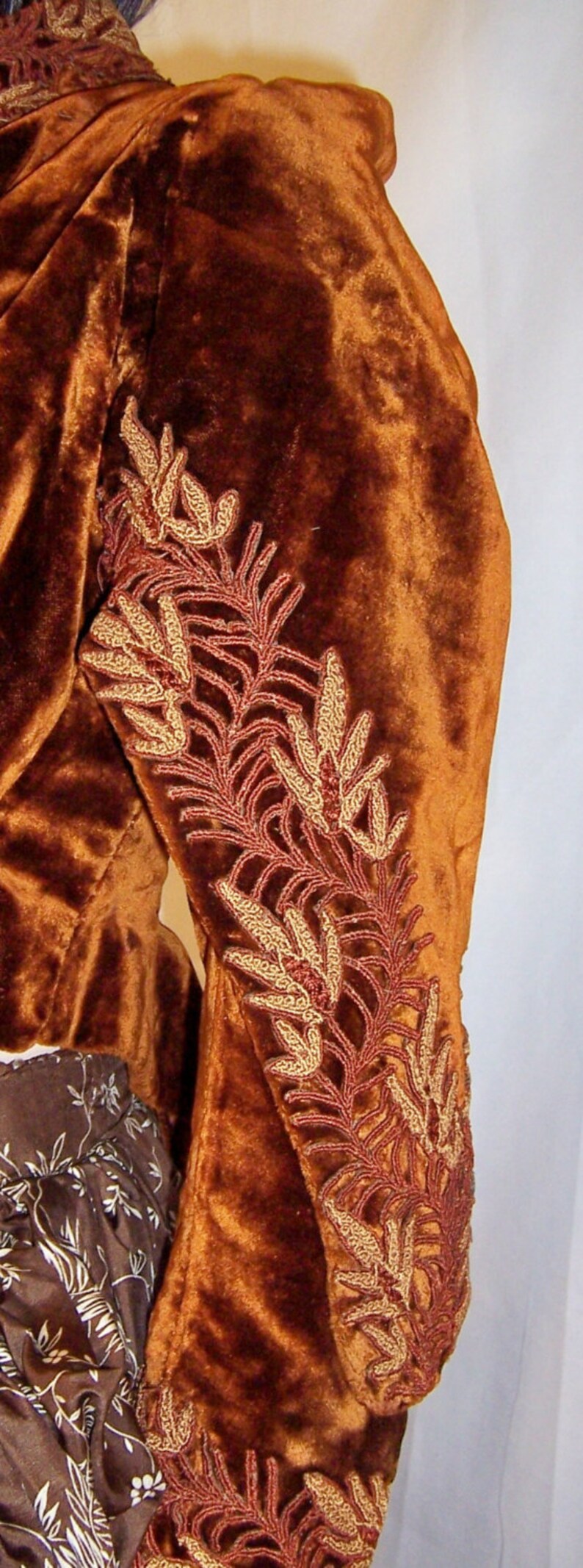 May include: A brown velvet jacket with gold and red embroidered floral designs on the sleeve.