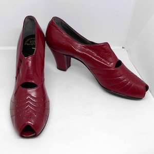 Puede incluir: Un par de zapatos de tacón rojo de cuero con puntera abierta y un diseño recortado, con una etiqueta de marca que dice "Fabriche Paris".