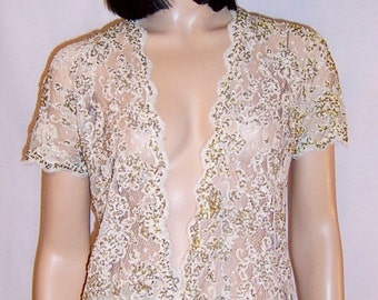 Puede incluir: Una blusa blanca de encaje con lentejuelas doradas, con un escote en V profundo y mangas cortas.