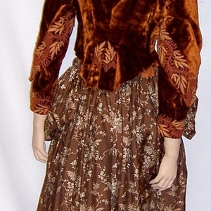 May include: A brown velvet jacket with gold embroidery over a brown skirt with a floral pattern.
