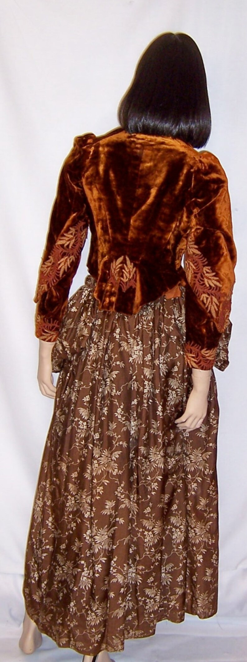 May include: A brown velvet jacket with gold embroidery over a brown skirt with a floral pattern.