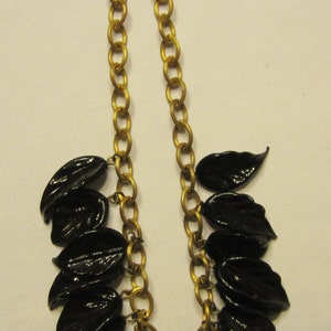 May include: A gold-tone chain necklace featuring glossy black leaf pendants. The necklace has a classic link chain design and a lobster clasp closure. The leaves are clustered at the front, creating a bold, elegant statement piece.