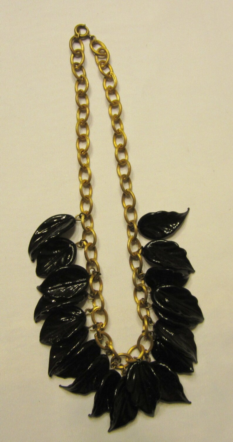 May include: A gold-tone chain necklace featuring glossy black leaf pendants. The necklace has a classic link chain design and a lobster clasp closure. The leaves are clustered at the front, creating a bold, elegant statement piece.
