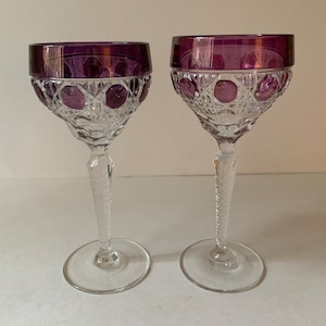 May include: Two clear glass wine glasses with a purple rim and cut glass design.