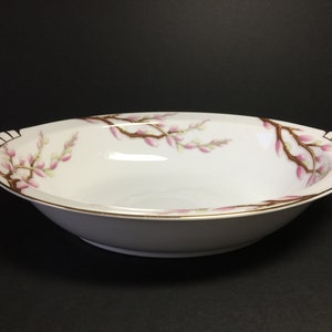 May include: A white oval serving bowl with a gold rim and a floral design of pink blossoms and brown branches.