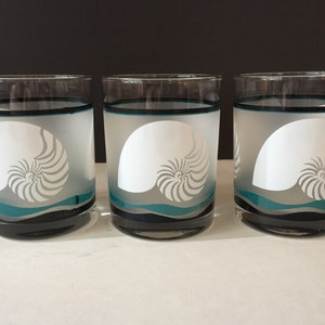 May include: Set of three frosted glass tumblers with a nautilus shell design. The glasses have a black rim and a blue and gray wave design.