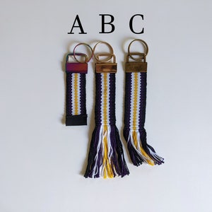 May include: Three purple, white, and gold striped keychains with gold key rings and tassels. The keychains are labeled A, B, and C.