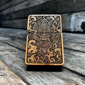 Pode incluir: Um isqueiro de madeira com um design gravado detalhado. O design apresenta um rosto estilizado com padrões intrincados e formas em espiral semelhantes a nuvens. O isqueiro é de uma cor de madeira natural quente com detalhes gravados em castanho escuro.