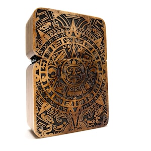 Puede incluir: Una caja de madera con una talla detallada del calendario azteca, también conocido como la Piedra del Sol. La talla es en negro y oro, y la caja está hecha de madera oscura.