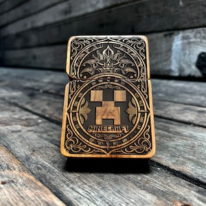 Może przedstawiać: Drewniany zapalniczka z misternym wzorem przedstawiającym twarz Creepera z Minecrafta i napis "Minecraft" w ozdobnym kroju pisma.