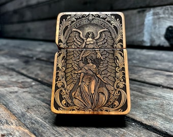 Pode incluir: Um isqueiro de metal dourado com um design gravado de um anjo com as asas abertas. O anjo é rodeado por padrões florais intrincados.