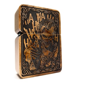 Könnte beinhalten: Ein Holzfeuerzeug mit einer detaillierten Gravur des Jokers aus Batman. Der Joker hält eine Waffe und die Worte "HA HA HA" sind um ihn herum graviert.
