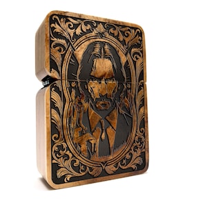 May include: A wooden lighter with an intricate engraved design featuring a portrait of a man with a serious expression. The design includes a floral pattern and a frame around the portrait.