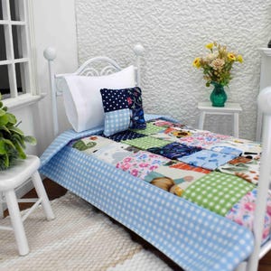 May include: Miniature white metal bed with a patchwork quilt in various colors and patterns. The bed has a blue gingham bed skirt and is accessorized with a white pillow and a patterned pillow. A small white chair and a rug are in the foreground.