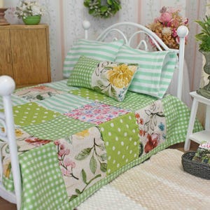 May include: A miniature white bed with a patchwork quilt in shades of green, white, and floral patterns. The bed has matching striped pillows and a decorative pillow with a yellow flower. A small rug and side table complete the scene.