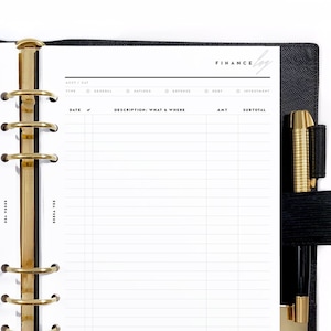 May include: Open black leather binder with gold-colored rings and a pen. The planner is open to a finance log page with the word "Finance" at the top. The pages have columns for date, description, amount, and subtotal.