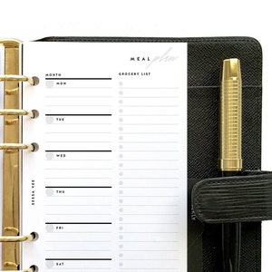 Könnte beinhalten: Ein schwarzer Leder-Planer mit goldenen Ringen und einem Stift. Der Planer hat ein wöchentliches Essensplan-Layout mit Abschnitten für Einkaufslisten und Essensideen. Der Text "MEAL plan" ist auf der Seite gedruckt.