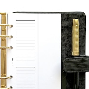 May include: A black leather bound planner with gold rings and a pen holder. The planner is open to a blank page with lined paper.