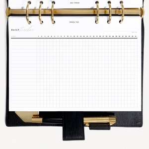 Könnte beinhalten: Ein weißer Tagesplaner mit einem Gittermuster und dem Wort "HABIT" oben gedruckt. Der Planer ist auf einer leeren Seite geöffnet, auf der die Zahlen 1 bis 31 oben gedruckt sind.