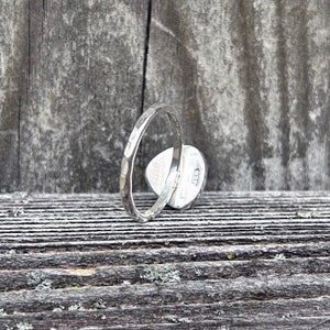 May include: A silver ring with a hammered texture. The ring is on a wooden surface.