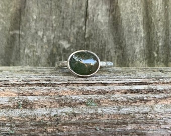 May include: A silver ring with a dark green oval-shaped stone set in the centre.