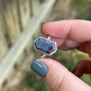 May include: A silver ring with a faceted, octagonal, blue and pink gemstone.