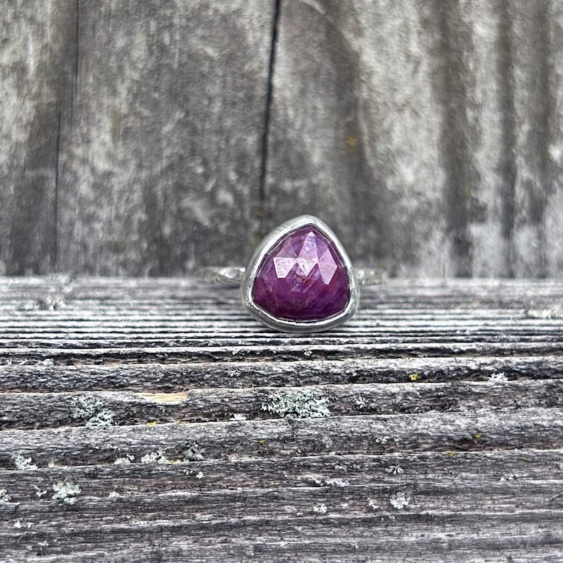 May include: A silver ring with a triangular purple gemstone set in the center.