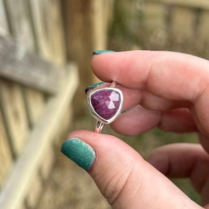 May include: A silver ring with a triangular, faceted, pink gemstone.