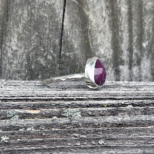 May include: A silver ring with a hammered band and a large, faceted, purple gemstone.