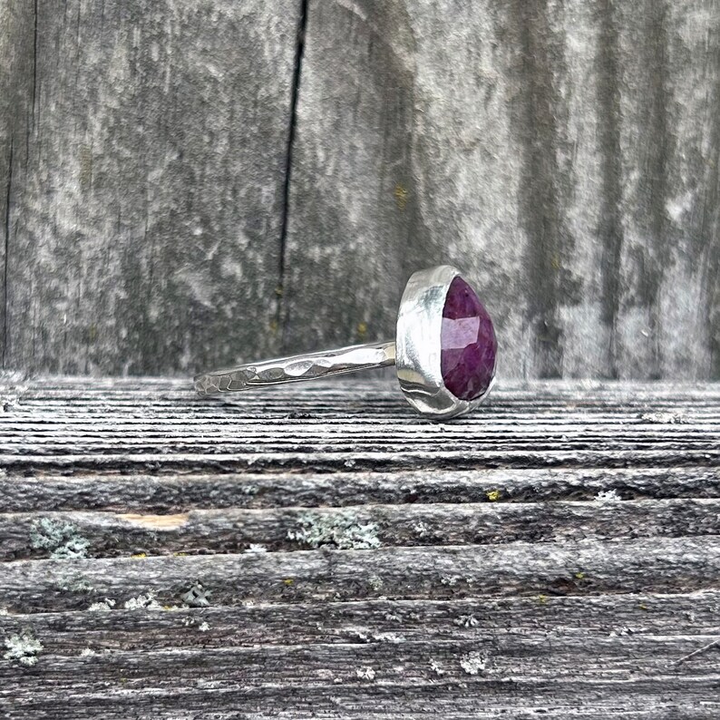 May include: A silver ring with a hammered band and a large, faceted, purple gemstone.