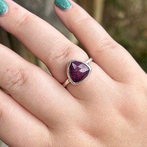 May include: A silver ring with a triangular purple gemstone set in a textured band.