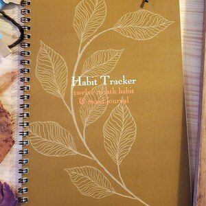 May include: A gold-colored spiral bound journal with a white leaf design and the text "Habit Tracker twelve month habit & mood journal".