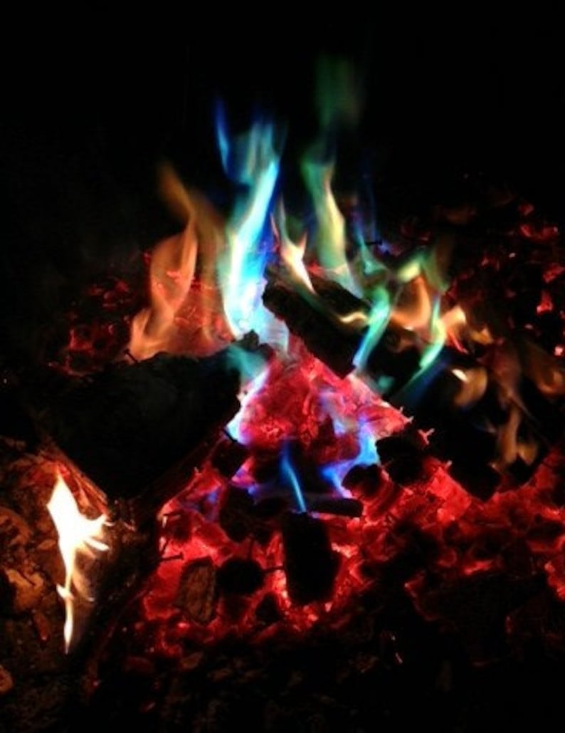 K&ouml;nnte beinhalten: Ein lebendiges Lagerfeuer mit Flammen in Blau-, Gr&uuml;n-, Orange- und Rott&ouml;nen. Das brennende Holz und die Glut leuchten vor einem dunklen Hintergrund und erzeugen eine farbenfrohe und dynamische Szene.