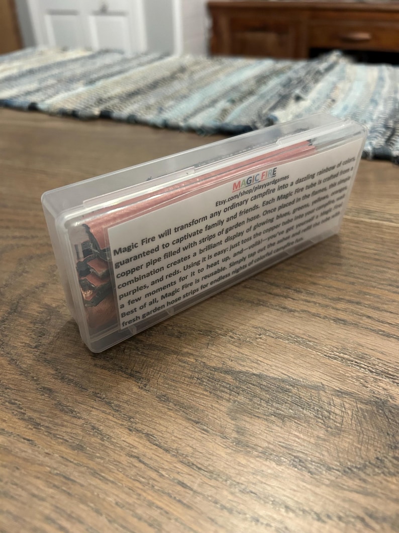 K&ouml;nnte beinhalten: Eine transparente Kunststoffbox mit Streifen aus Gartenschlauch f&uuml;r Lagerfeuer. Auf der Box steht "MAGIC FIRE" und eine Produktbeschreibung. Die Streifen erzeugen ein farbenfrohes Flammenspiel.