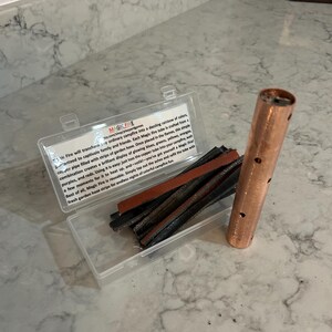 K&ouml;nnte beinhalten: Eine transparente Kunststoffbox mit Gartenschlauchstreifen und einem Kupferrohr mit L&ouml;chern. Der Text auf der Box lautet "MAGIC FIRE" und beschreibt, wie das Produkt eine farbenfrohe Lagerfeueranzeige erzeugt.