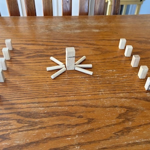 May include: A wooden game with a tower of blocks in the center and surrounding blocks arranged in a circle. The blocks are all natural wood color.
